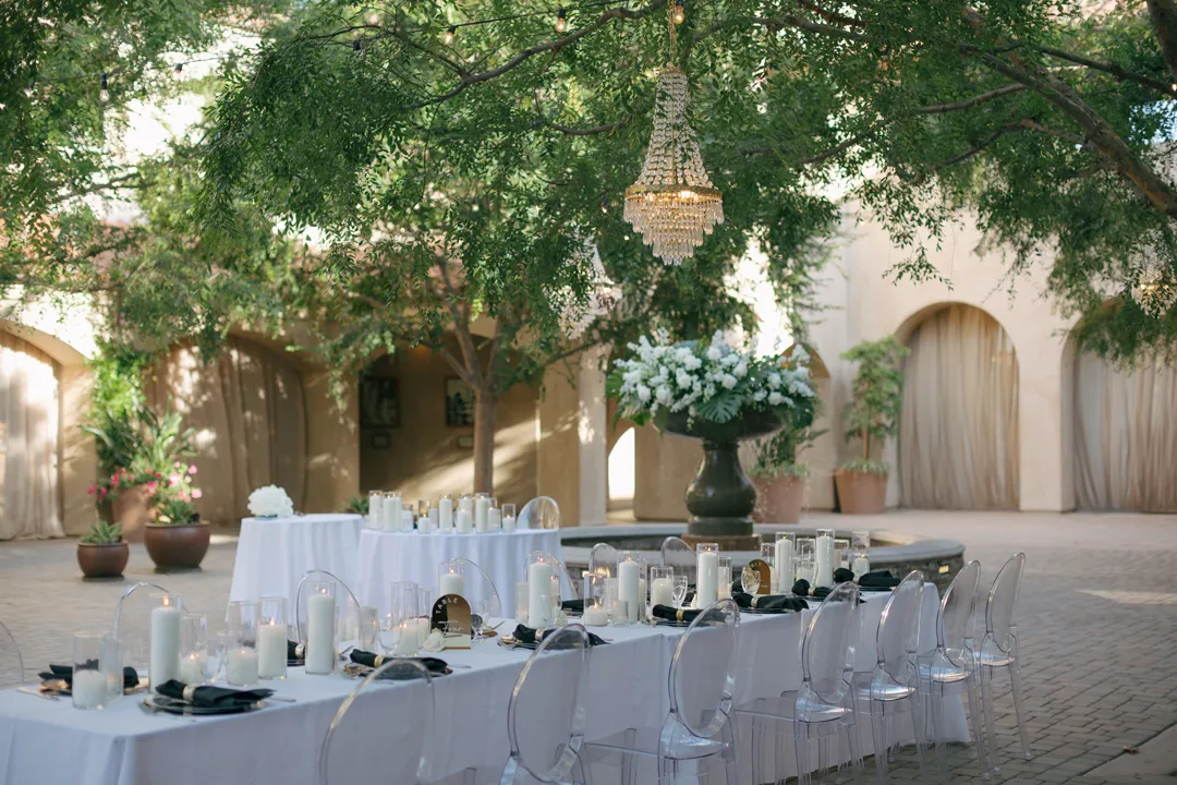 Courtyard reception tables with clear chairs and pillar candles.