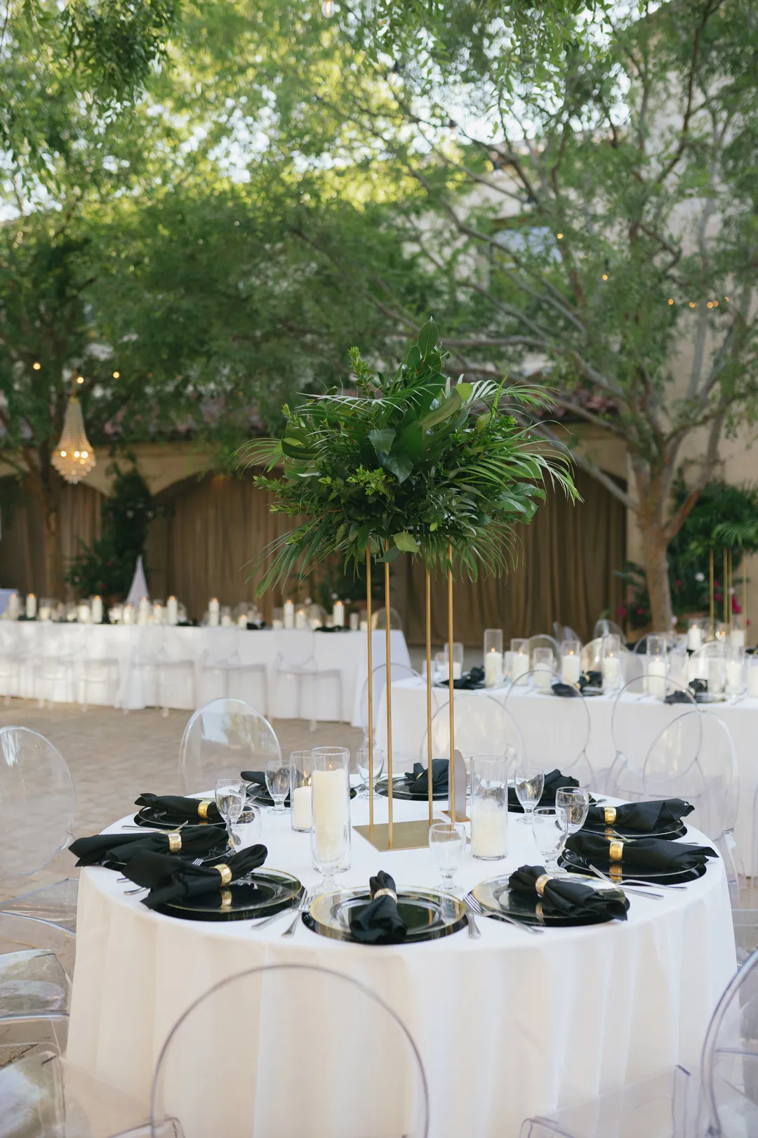 Round reception table with tropical greenery and black napkins.