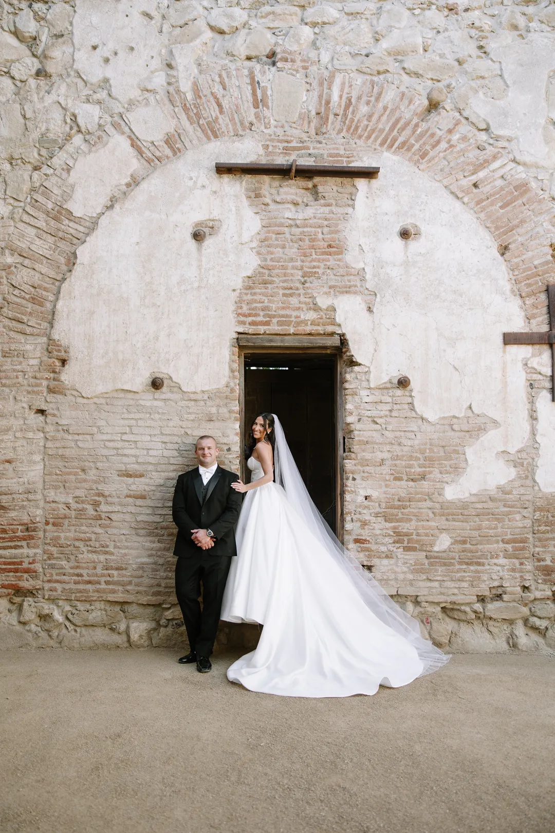 Wedding couple posing beside an old brick doorway.