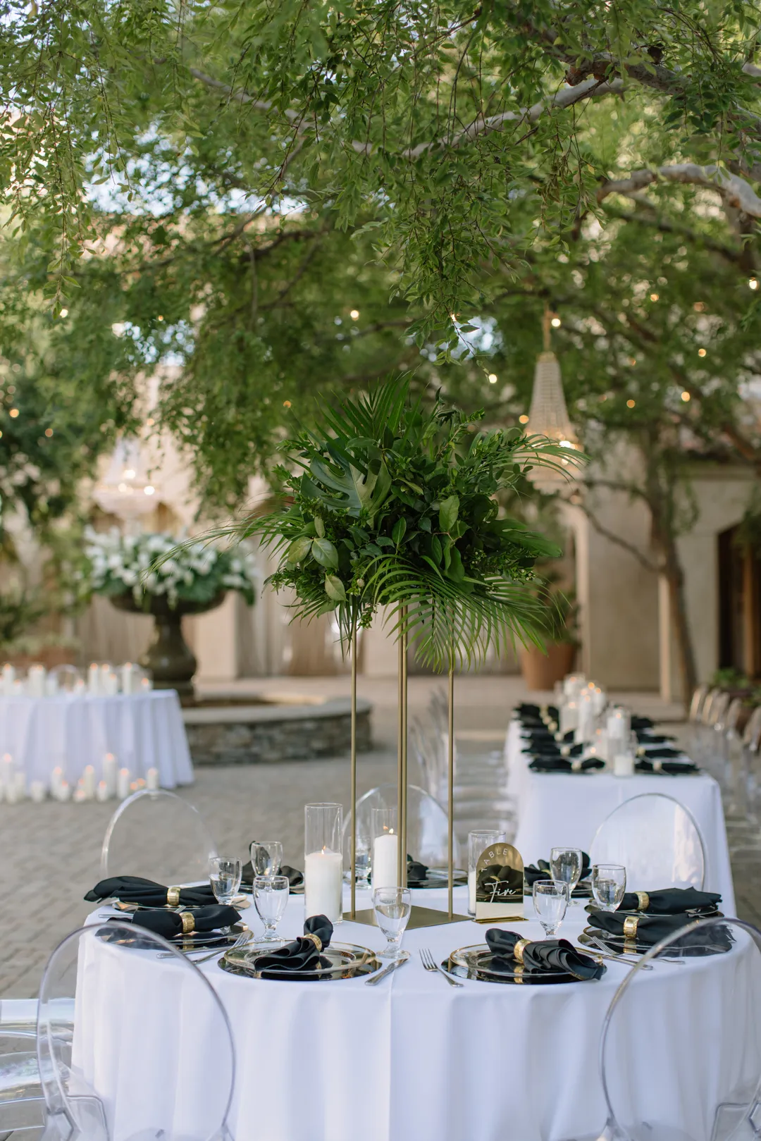 Tall tropical greenery centerpiece above a white-linen table.