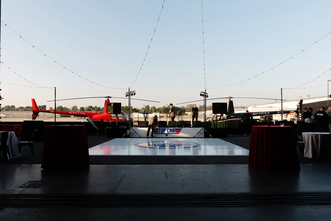 Outdoor party setup with an aviation-themed dance floor, string lights and a red helicopter.