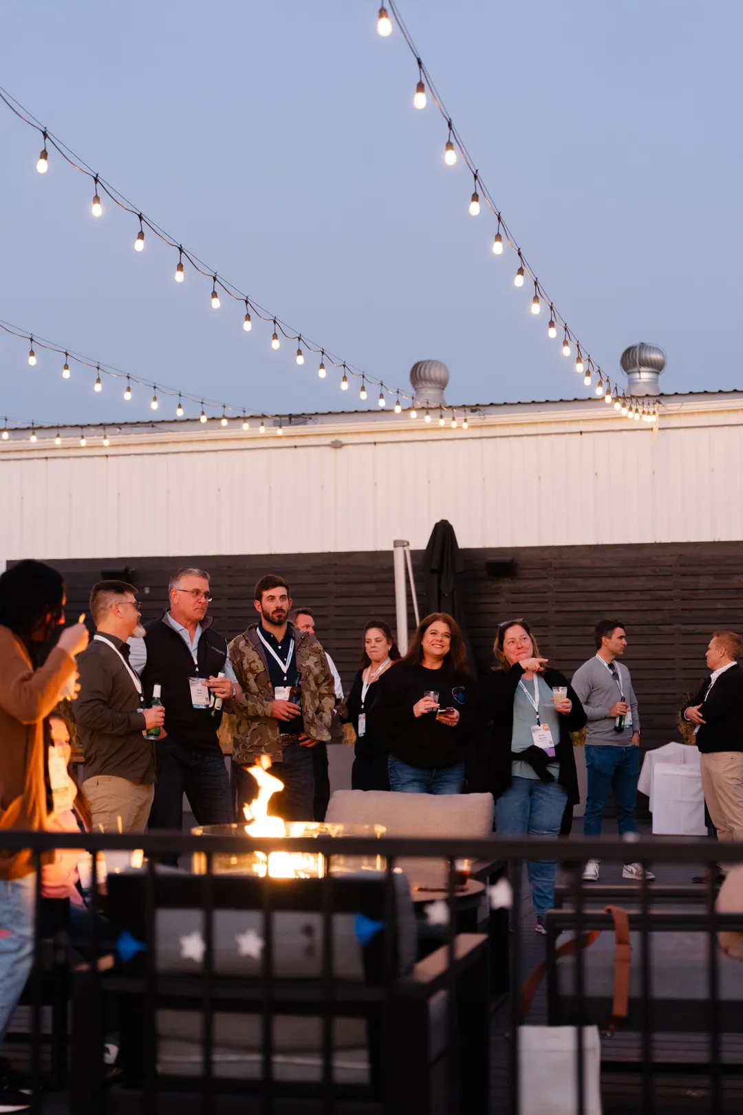 Guests gathered around an outdoor fire feature beneath string lights.