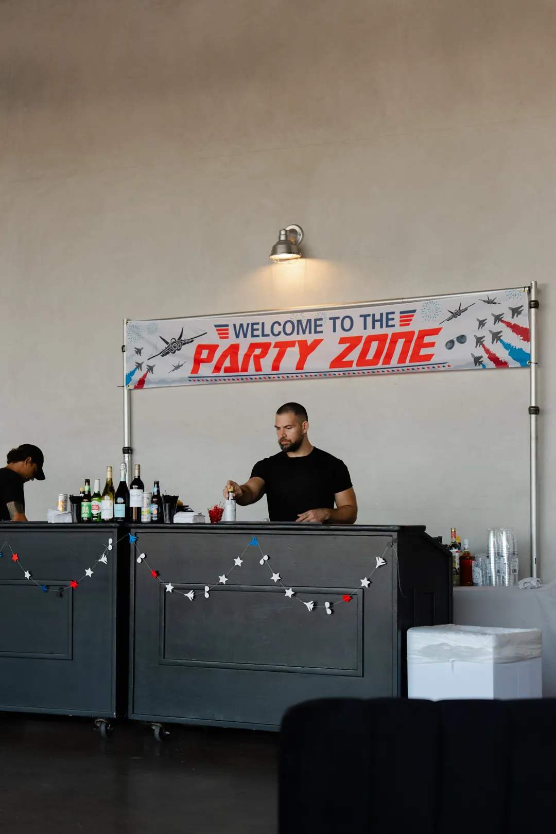 Bartender beneath a Welcome to the Party Zone banner.