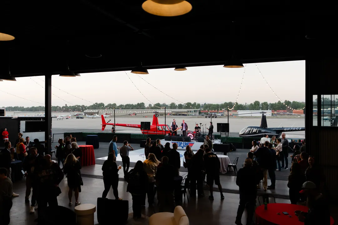 View through the open hangar toward patio guests and a red helicopter.