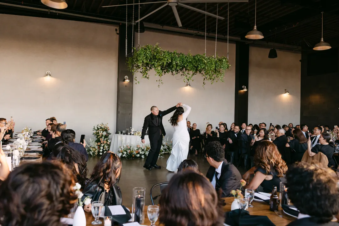 Newlyweds dancing beneath suspended greenery inside the hangar.