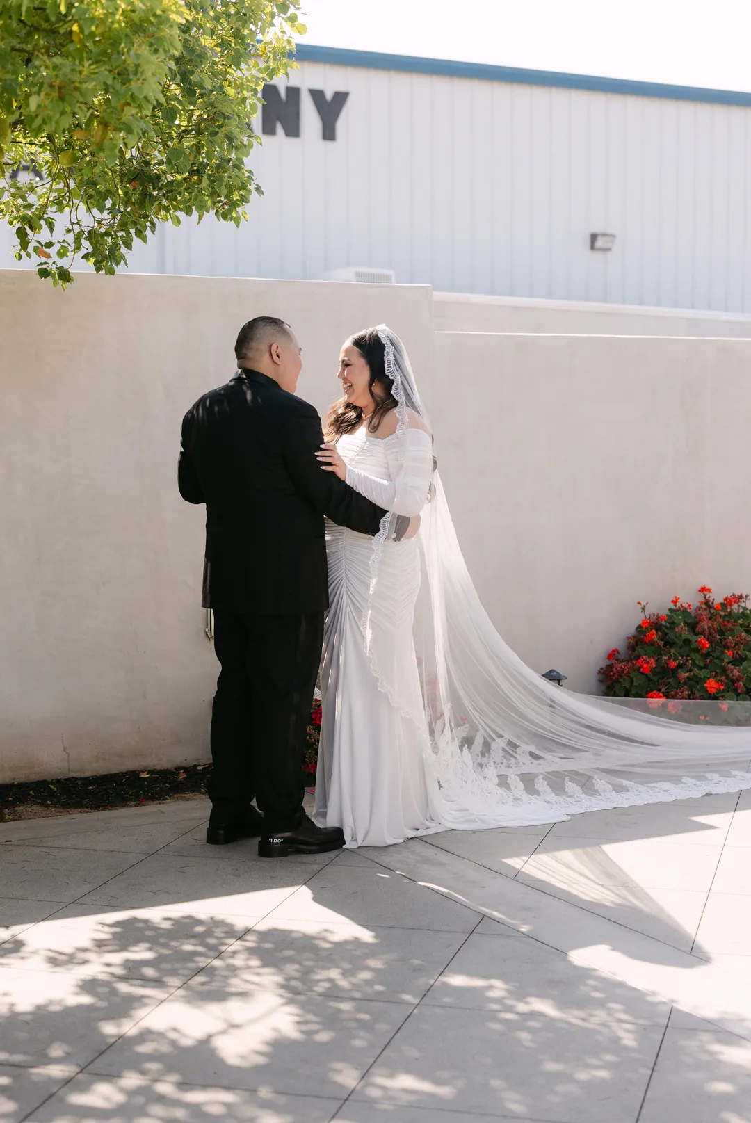 Wedding couple facing one another beneath a courtyard tree.