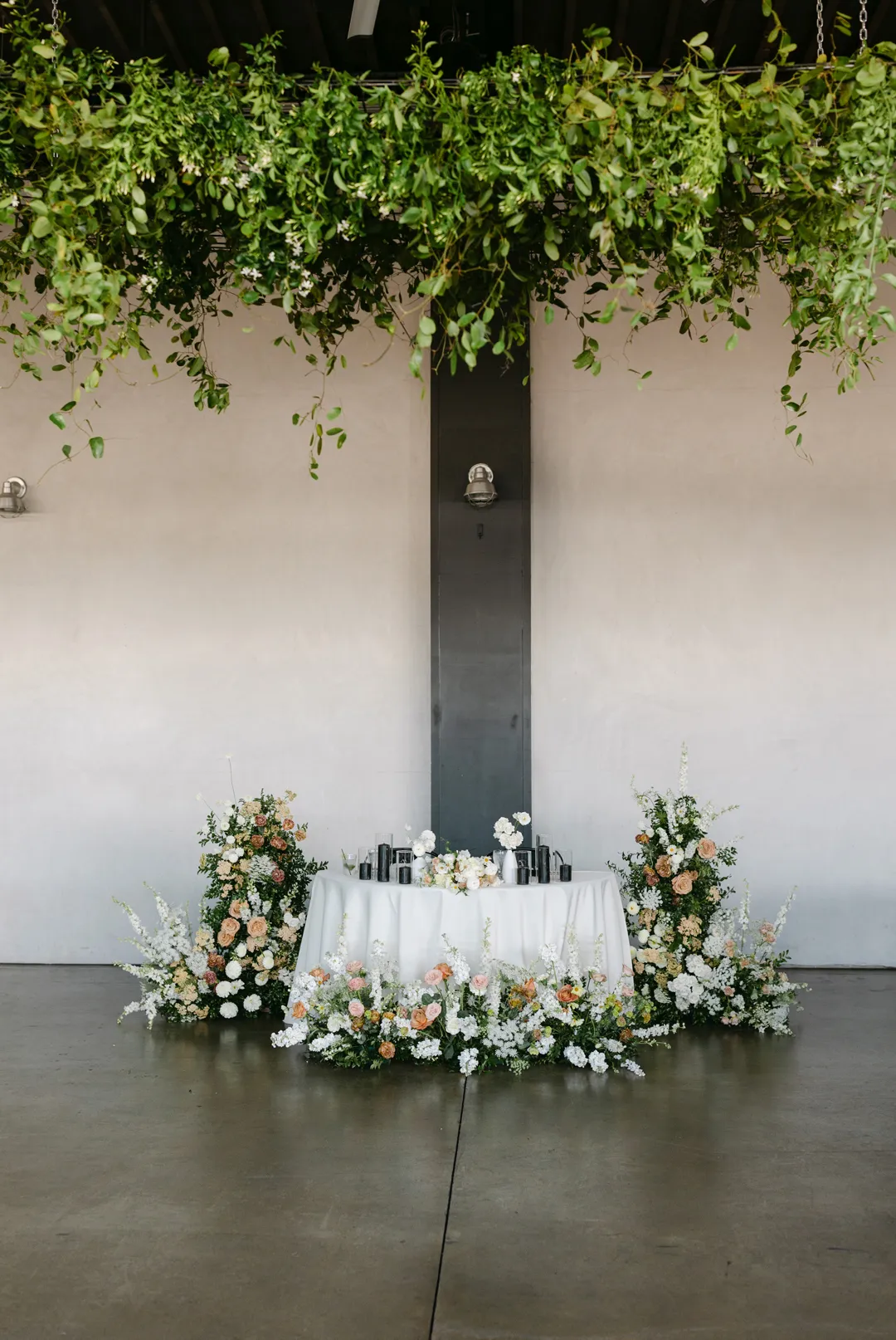 Floral sweetheart table beneath a suspended greenery arrangement.