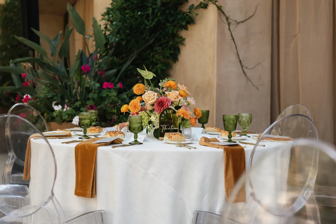 Round reception table with orange flowers, green goblets and golden napkins.