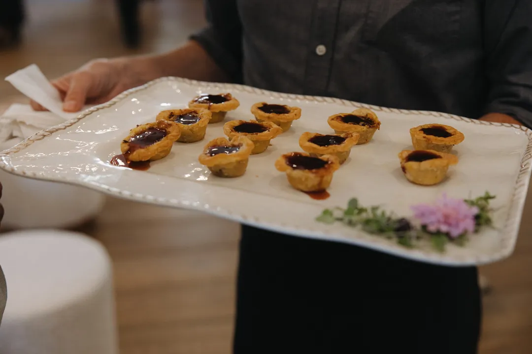 Server carrying a tray of miniature savory tarts.
