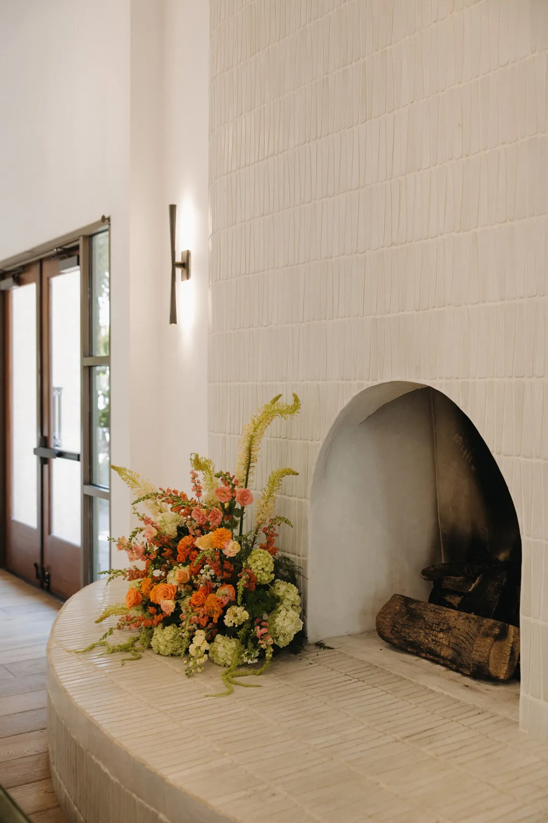 Orange and yellow flowers beside an arched white fireplace.