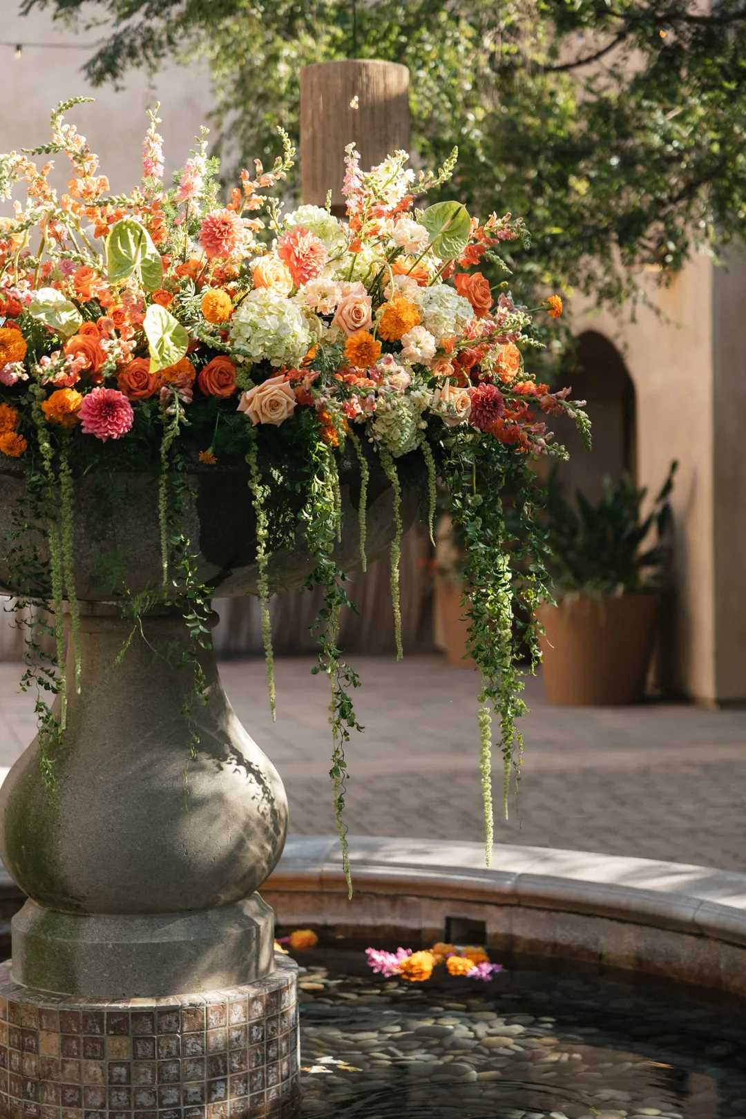 Orange and peach floral arrangement with trailing greenery on the fountain.