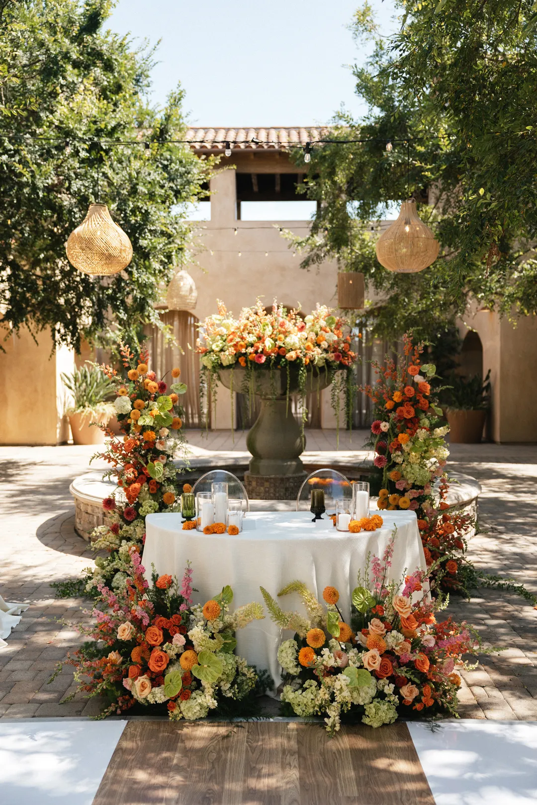 Sweetheart table framed by orange and yellow flowers beside the courtyard fountain.