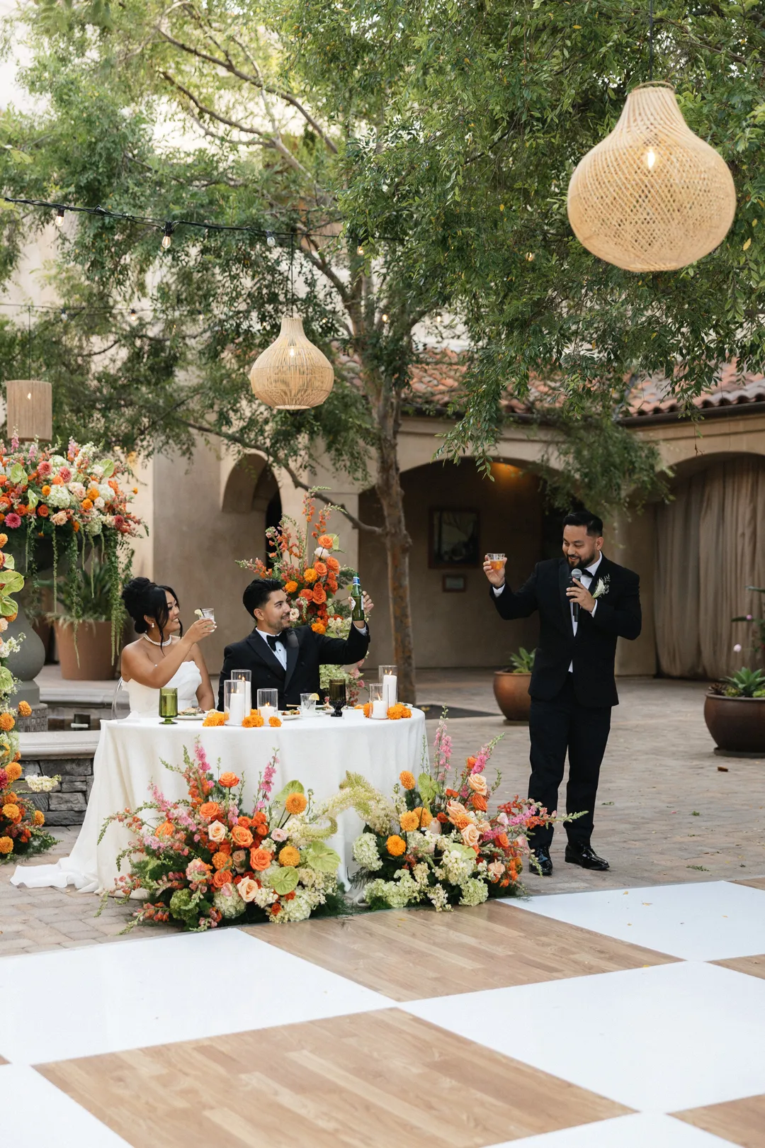 Wedding guest giving a toast beside the floral sweetheart table.