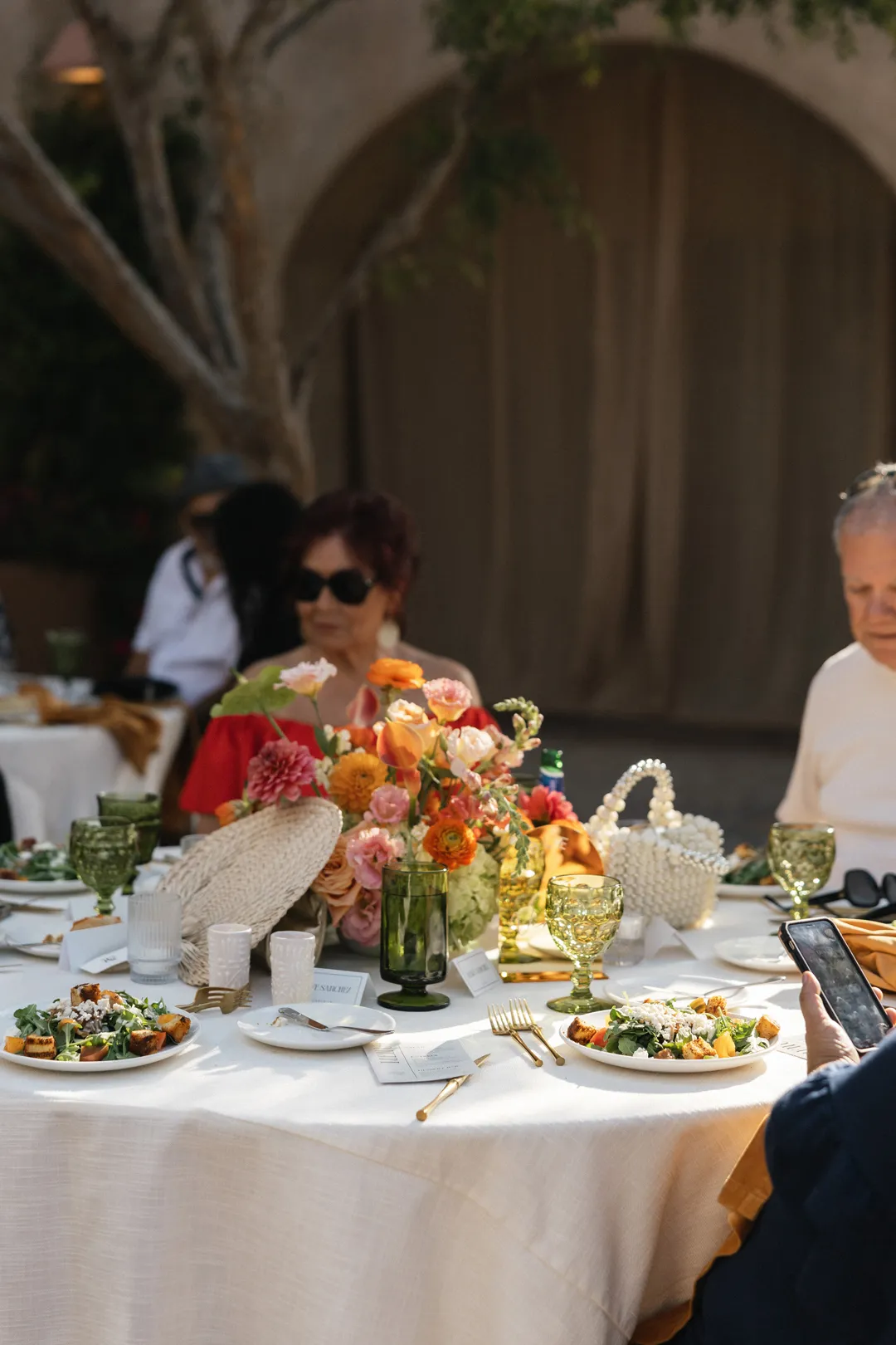 Guests seated at a reception table with orange flowers and green glassware.