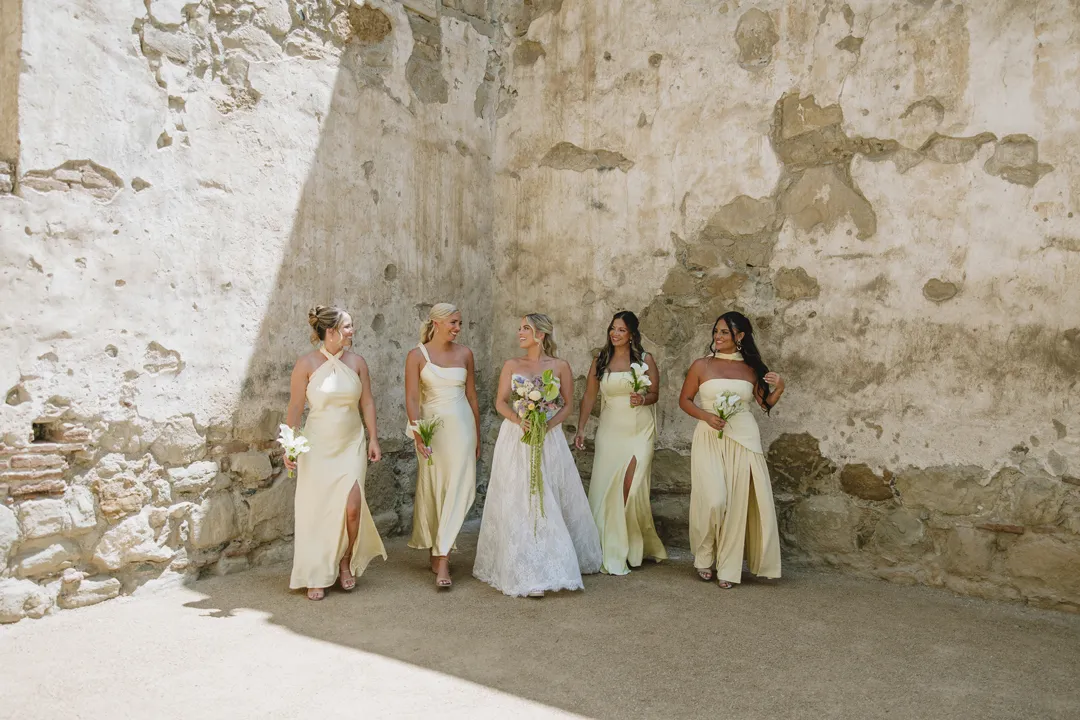Bride and bridesmaids in butter-yellow dresses at Mission San Juan Capistrano.