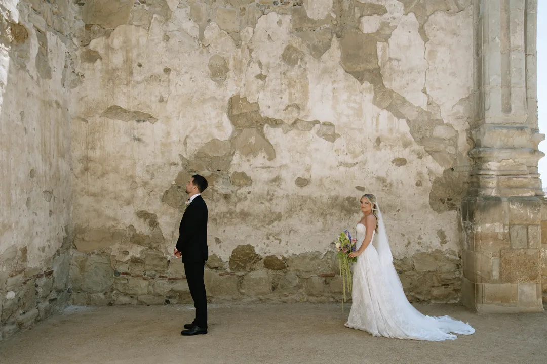 Bride approaching the groom for a first look at Mission San Juan Capistrano.