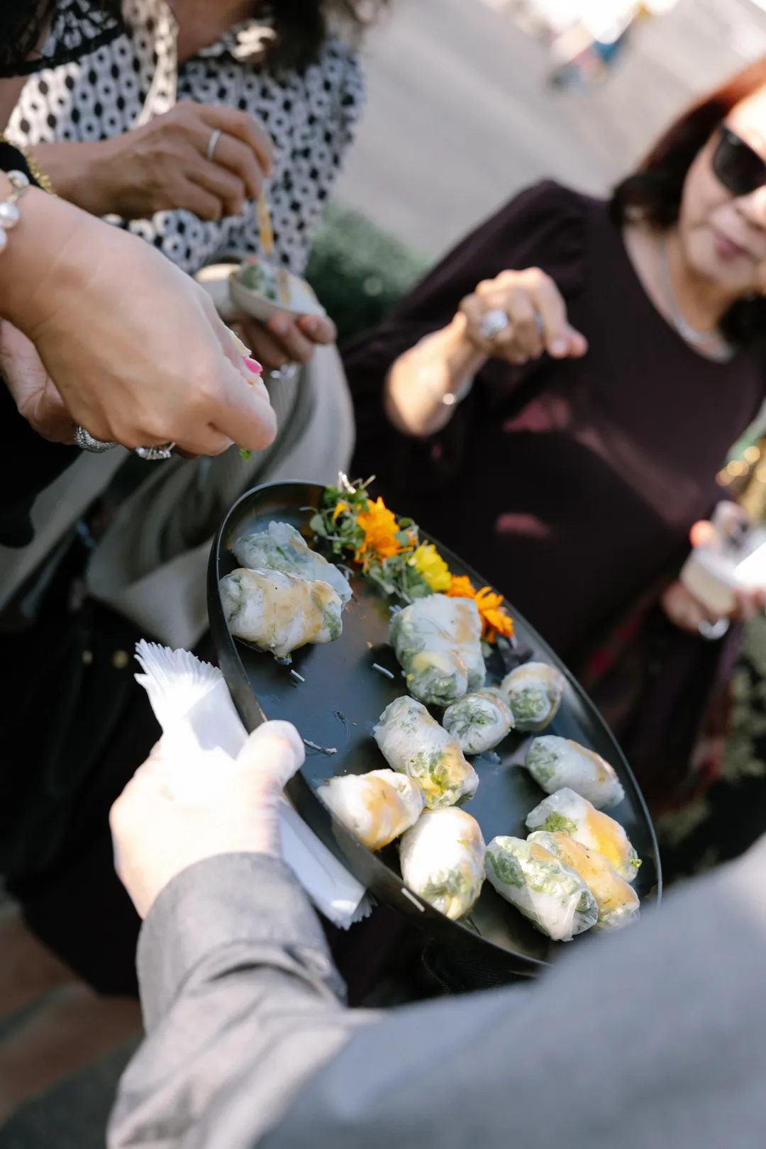 Guests selecting Jay's Catering Sesame Shrimp and Mango Spring Rolls from a tray.