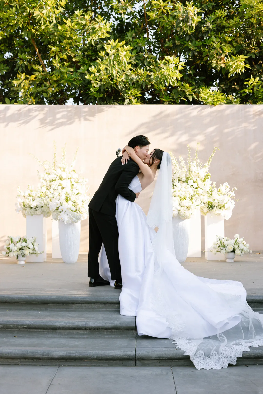 Newlyweds kissing between white floral arrangements at Hangar 21 South.
