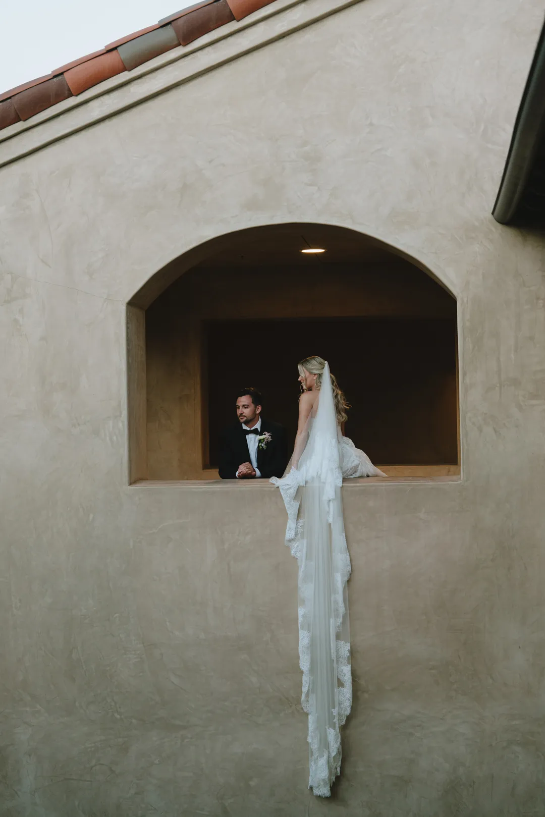 Wedding couple in a Serra Plaza balcony opening with the bride's veil draped below.