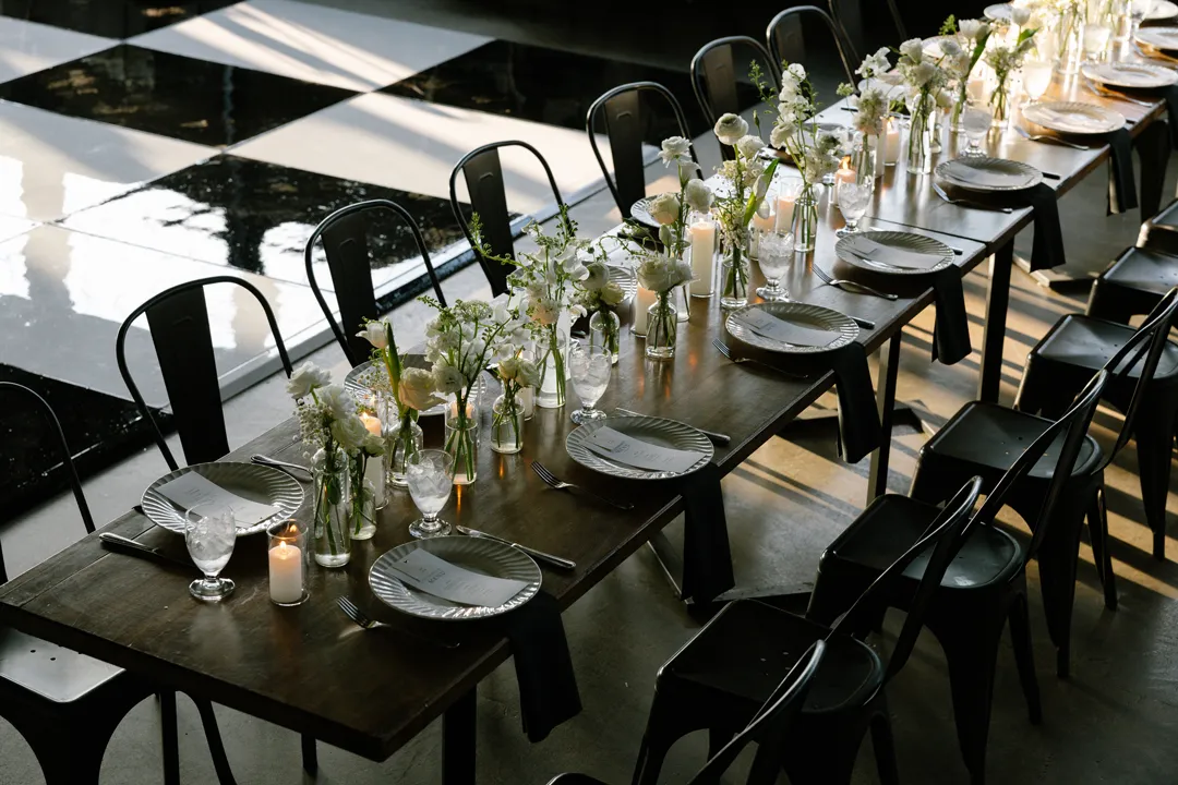 Long reception table with white flowers beside Hangar 21 South's checkered dance floor.