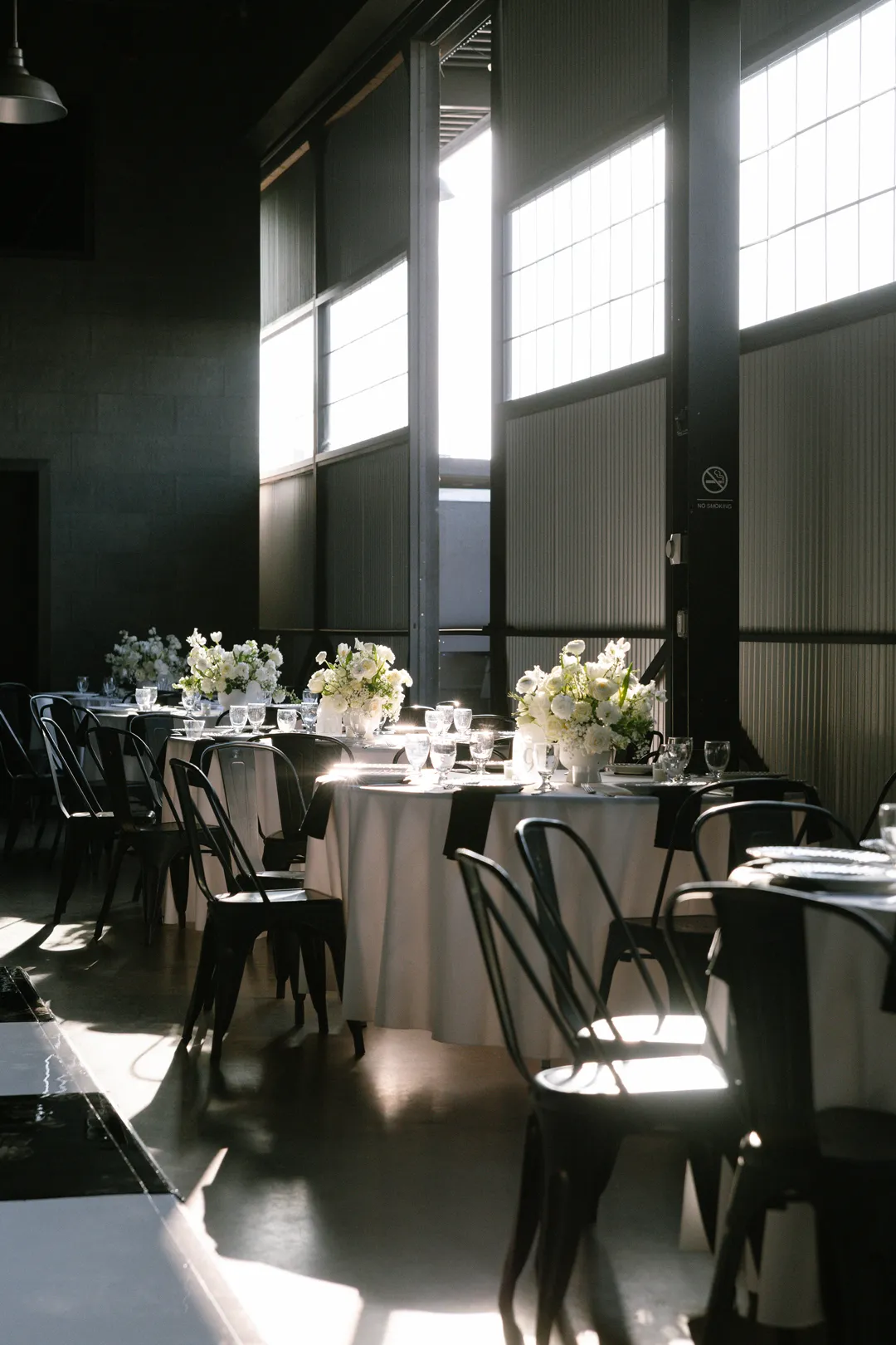 White-floral reception tables beside the tall Hangar 21 South windows.