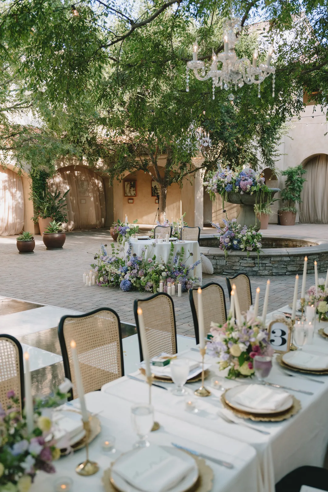 Serra Plaza reception table with purple and green flowers, candles and cane-backed chairs.