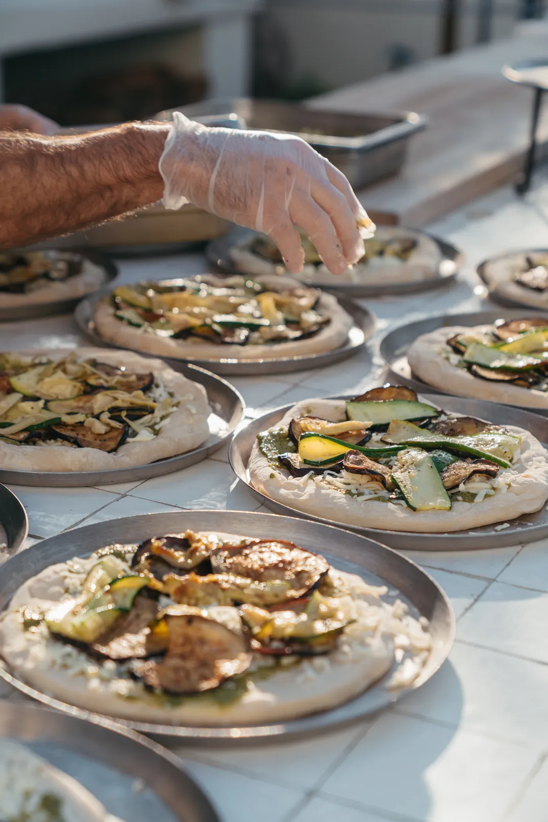 Jay's Catering staff adding toppings to Mediterranean Veggie Pizzas.