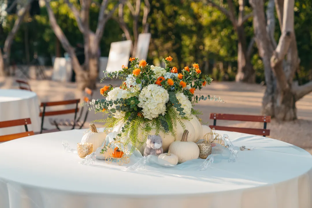 White and orange floral centerpiece with pumpkins at CHOC Guild Con.