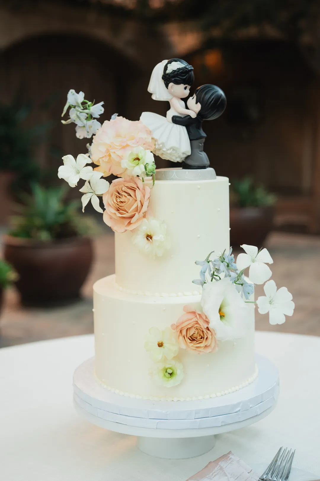 Jay's Catering two-tier wedding cake with peach flowers and a couple figurine topper.