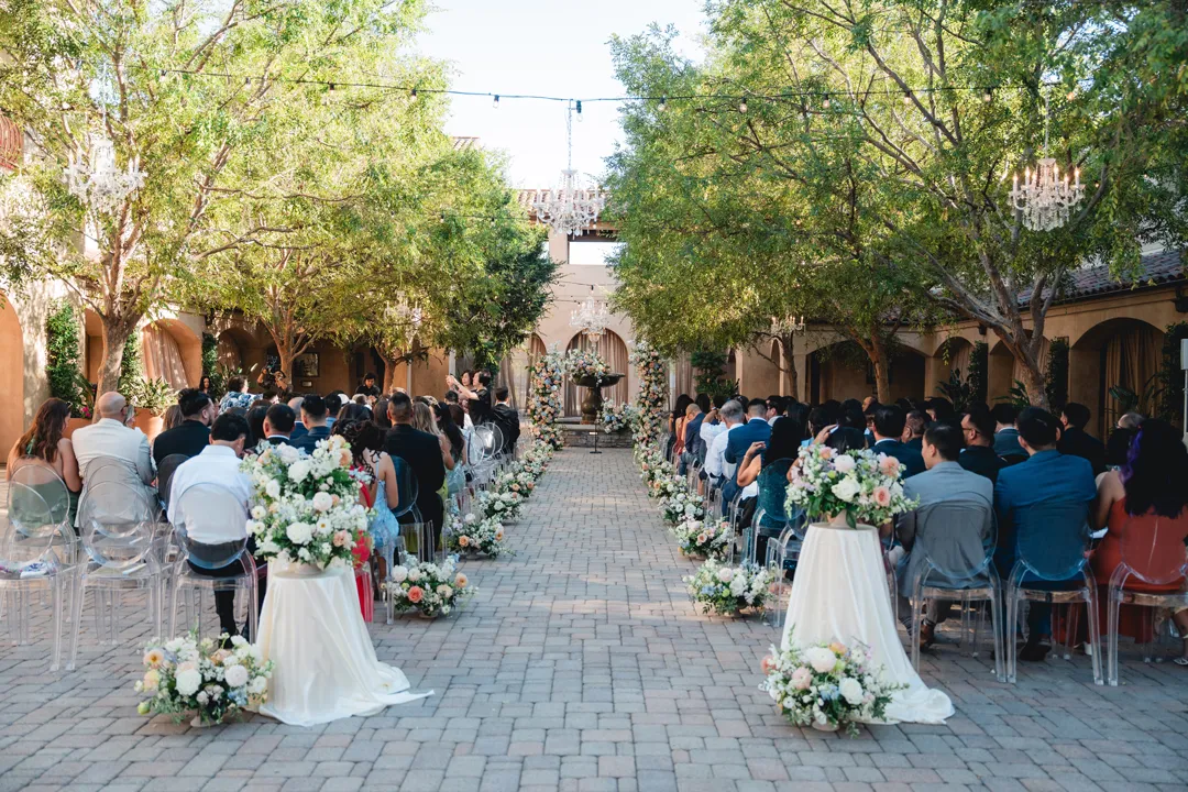 Guests seated for a wedding ceremony beneath the Serra Plaza courtyard trees.