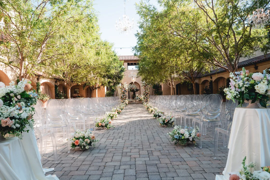 Serra Plaza courtyard ceremony aisle with clear chairs and peach, blue and white flowers.