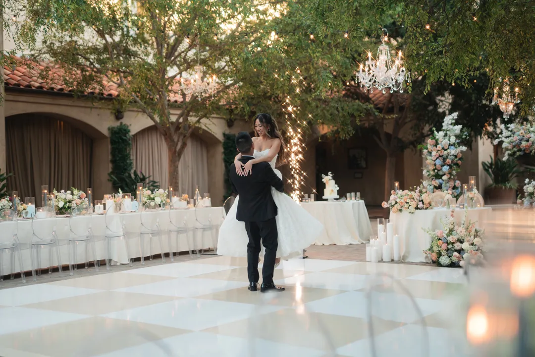 Groom lifting the bride during their first dance at Serra Plaza, with spark fountains behind them.