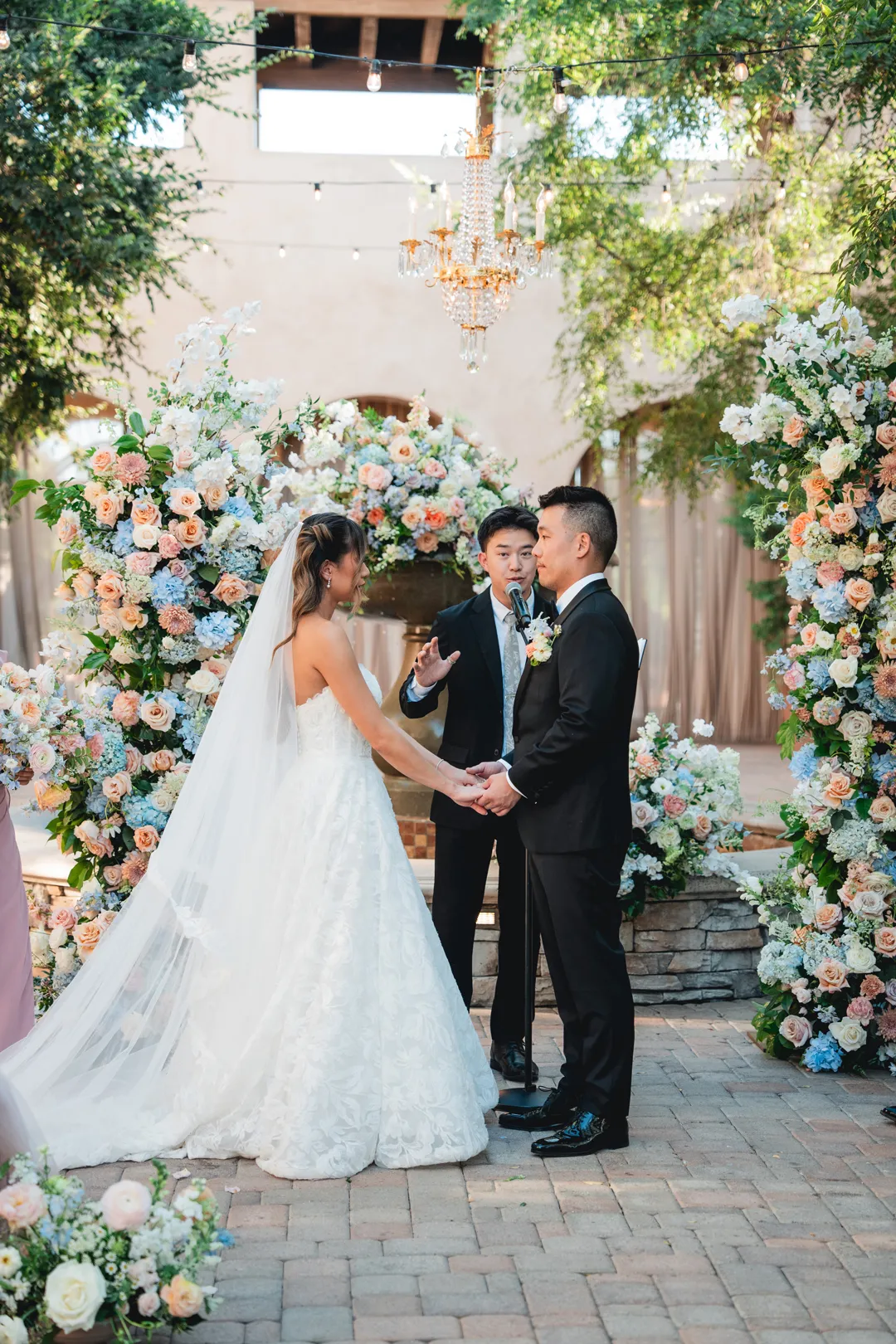 Wedding couple holding hands between pastel floral arrangements at their Serra Plaza ceremony.