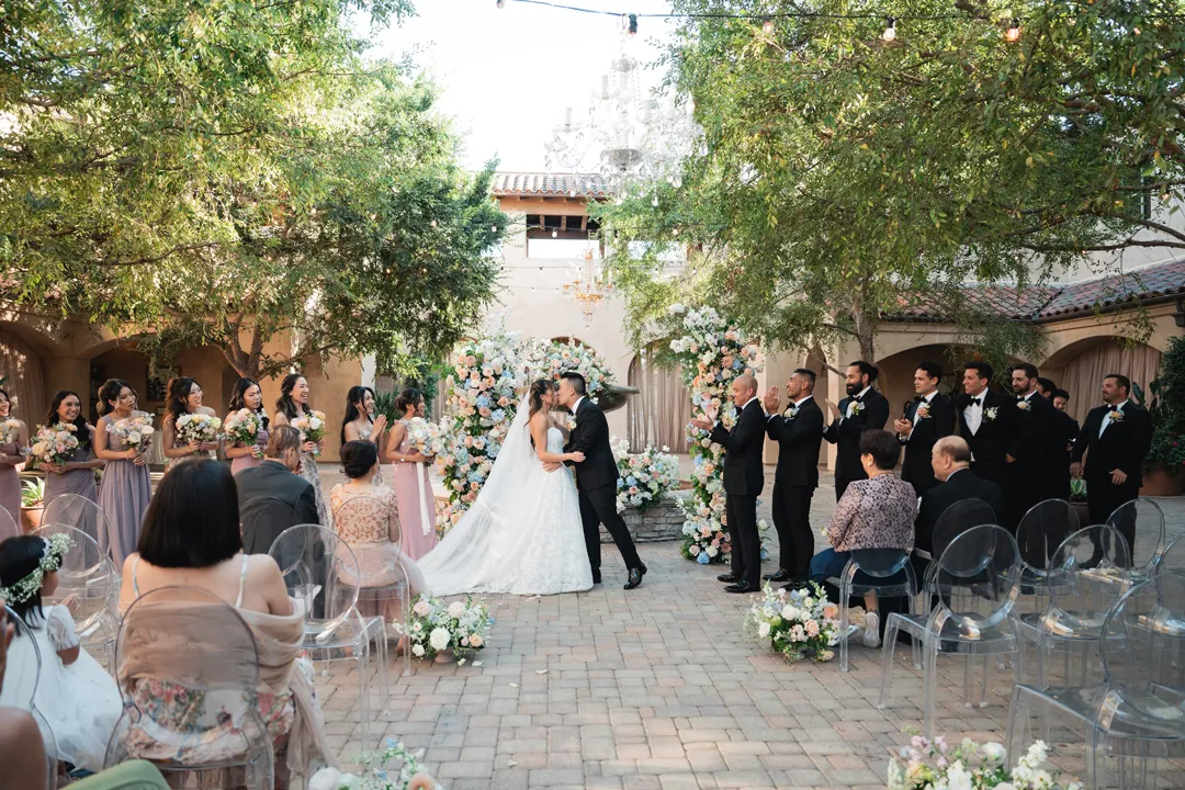 Groom dipping the bride for a kiss as the wedding party applauds.
