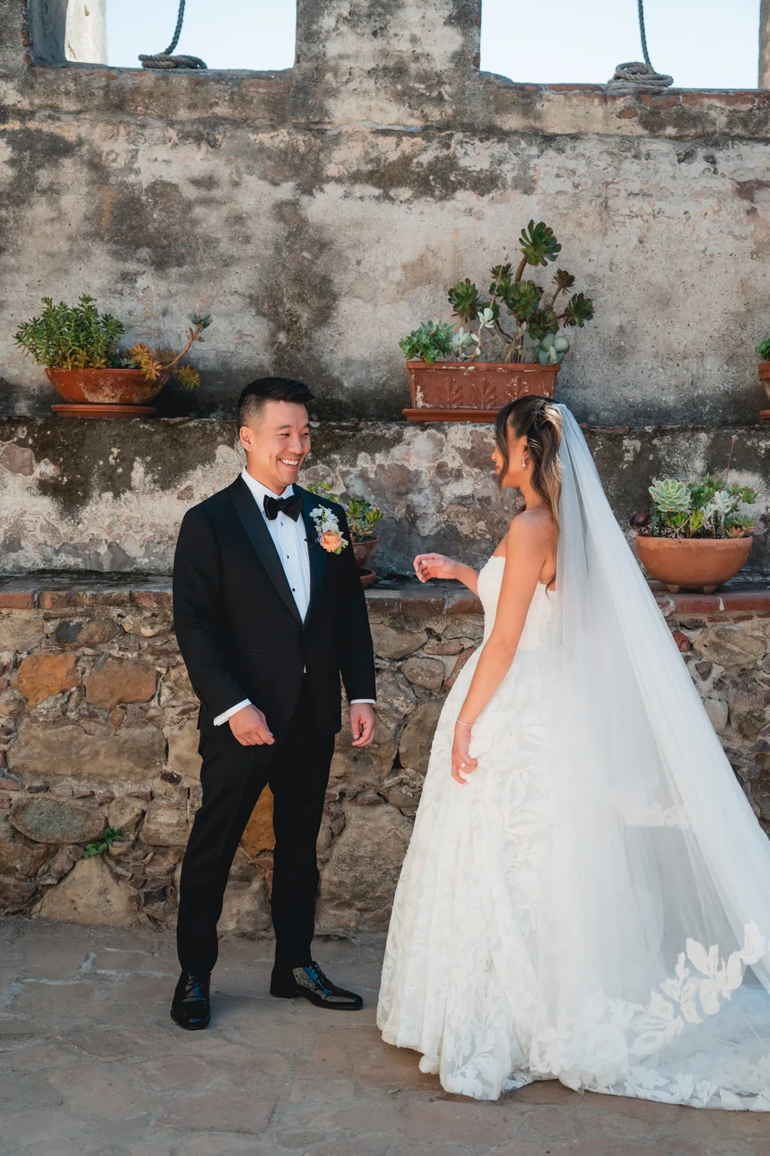 Wedding couple smiling beside potted plants in Mission San Juan Capistrano's Sacred Garden.