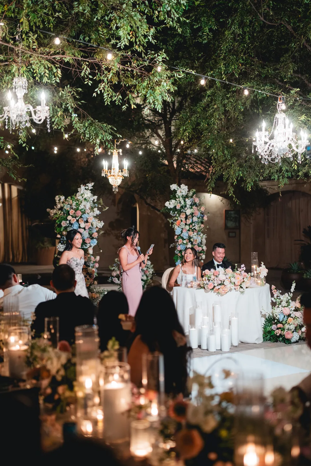 Guests giving a speech beside the sweetheart table at night.