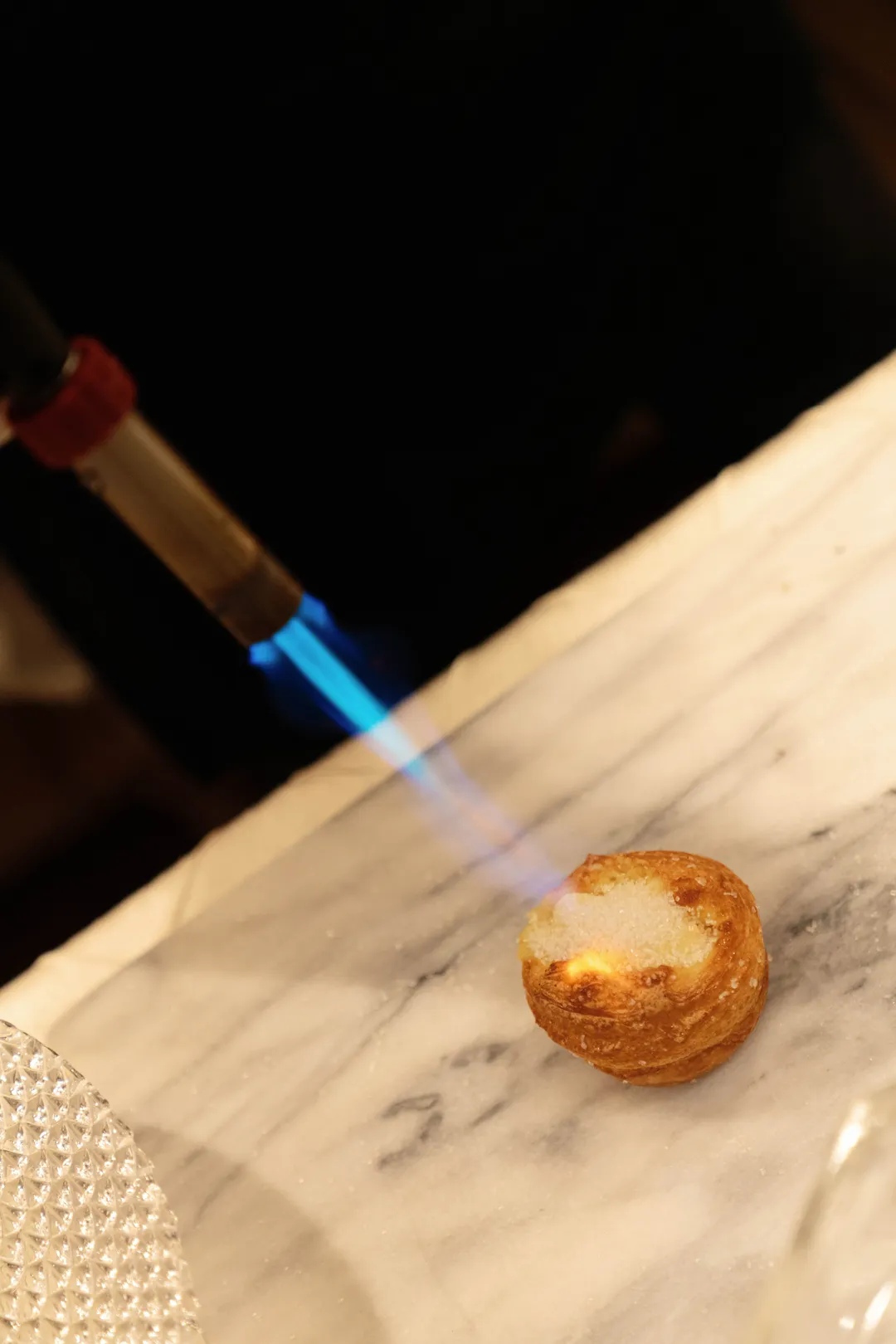 Close-up of a kitchen torch caramelizing a Kouign Amann pastry.