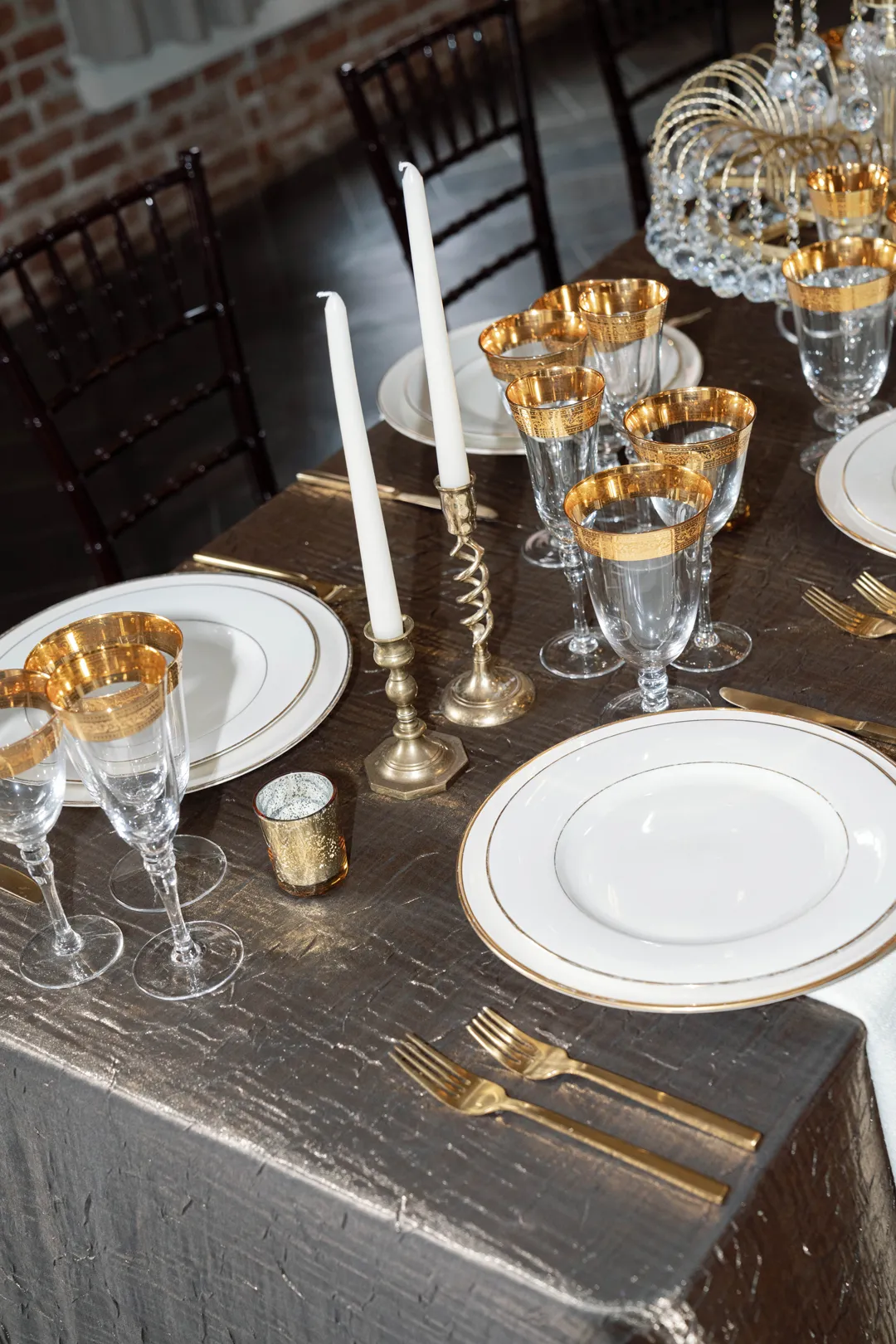 White plates, gold-rimmed glasses and taper candles on shimmering table linen.