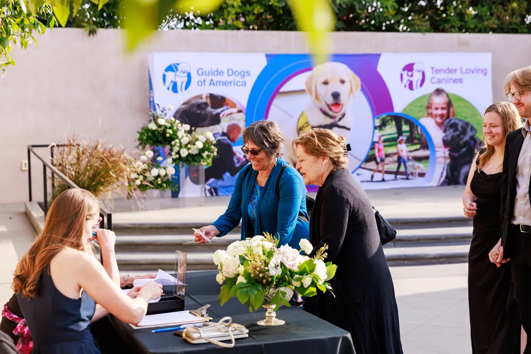 Guests checking in beside a Guide Dogs of America and Tender Loving Canines event banner.