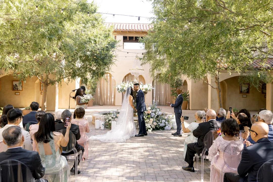 Newlyweds kissing beside the Serra Plaza fountain as guests applaud.