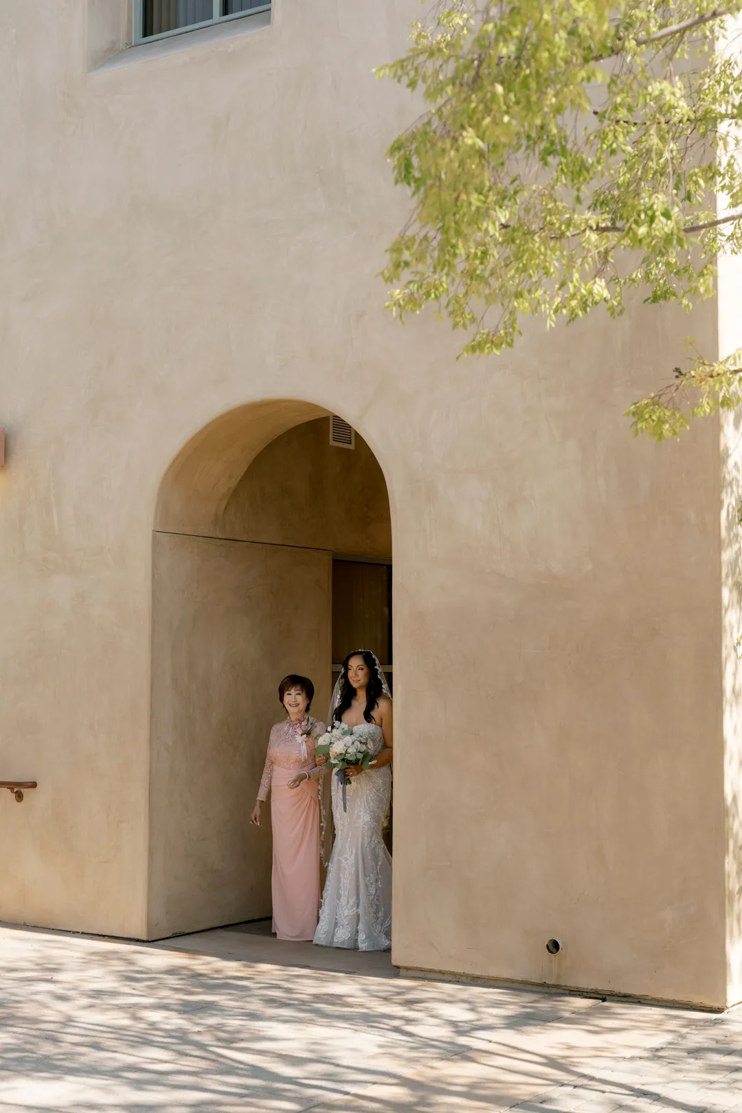 Bride and a companion waiting beneath an arch before the Serra Plaza ceremony.