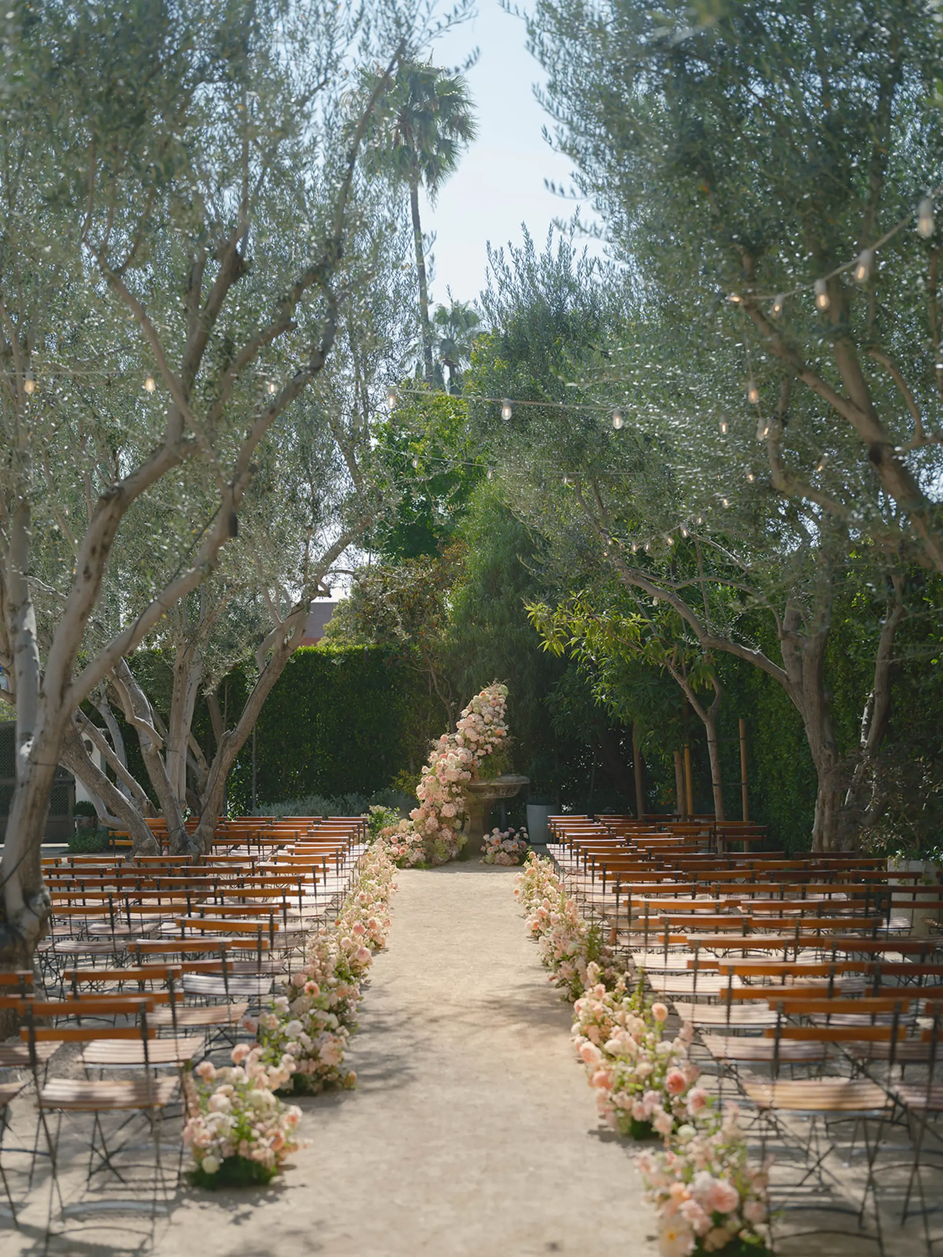 Blush floral arrangements line the wedding ceremony aisle and at the head, more florals decorate the original fountain backdrop.
