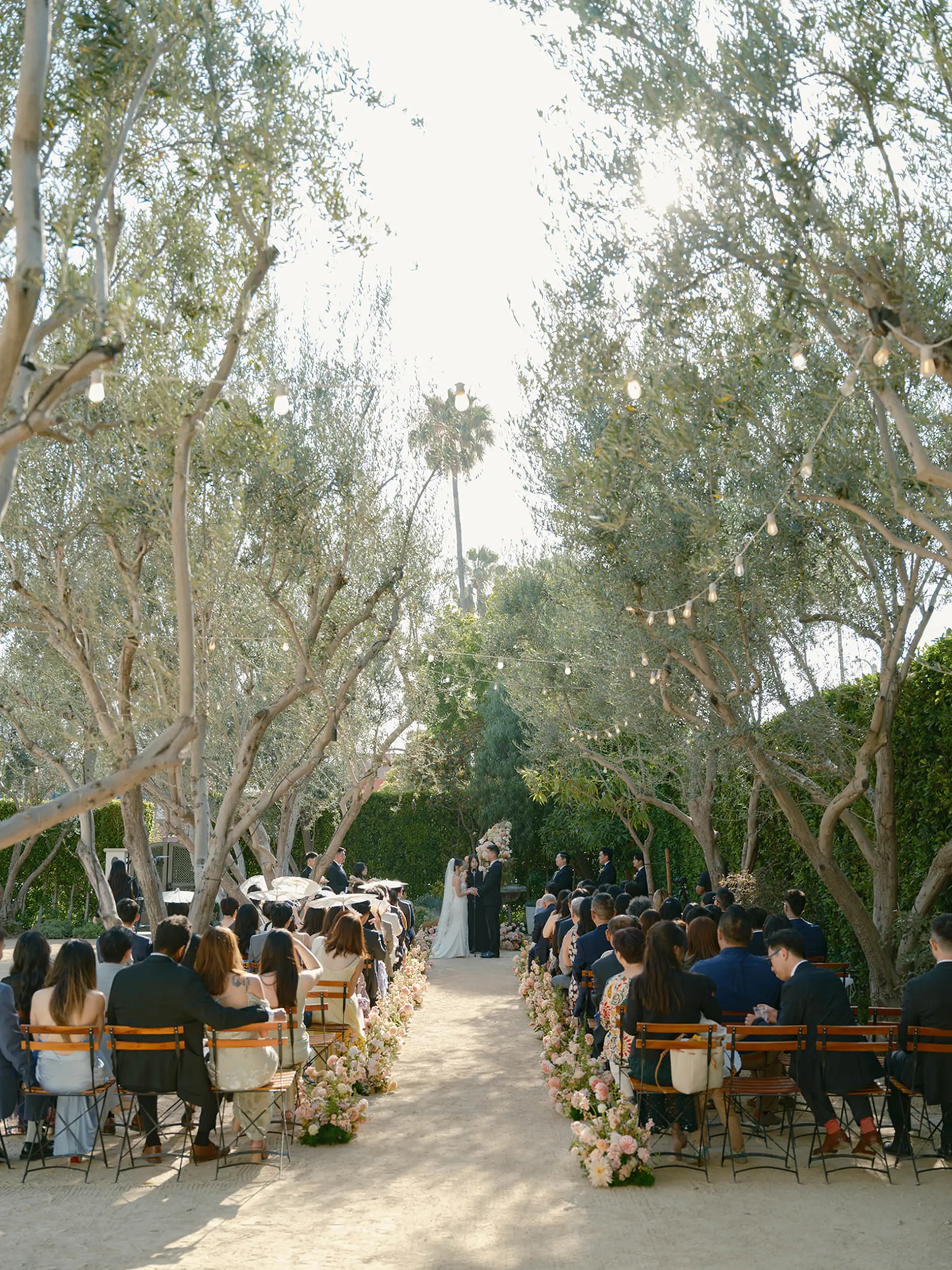 Blush floral arrangements line the aisle leading to the bride and groom reciting their wedding vows outside at Grand Gimeno.