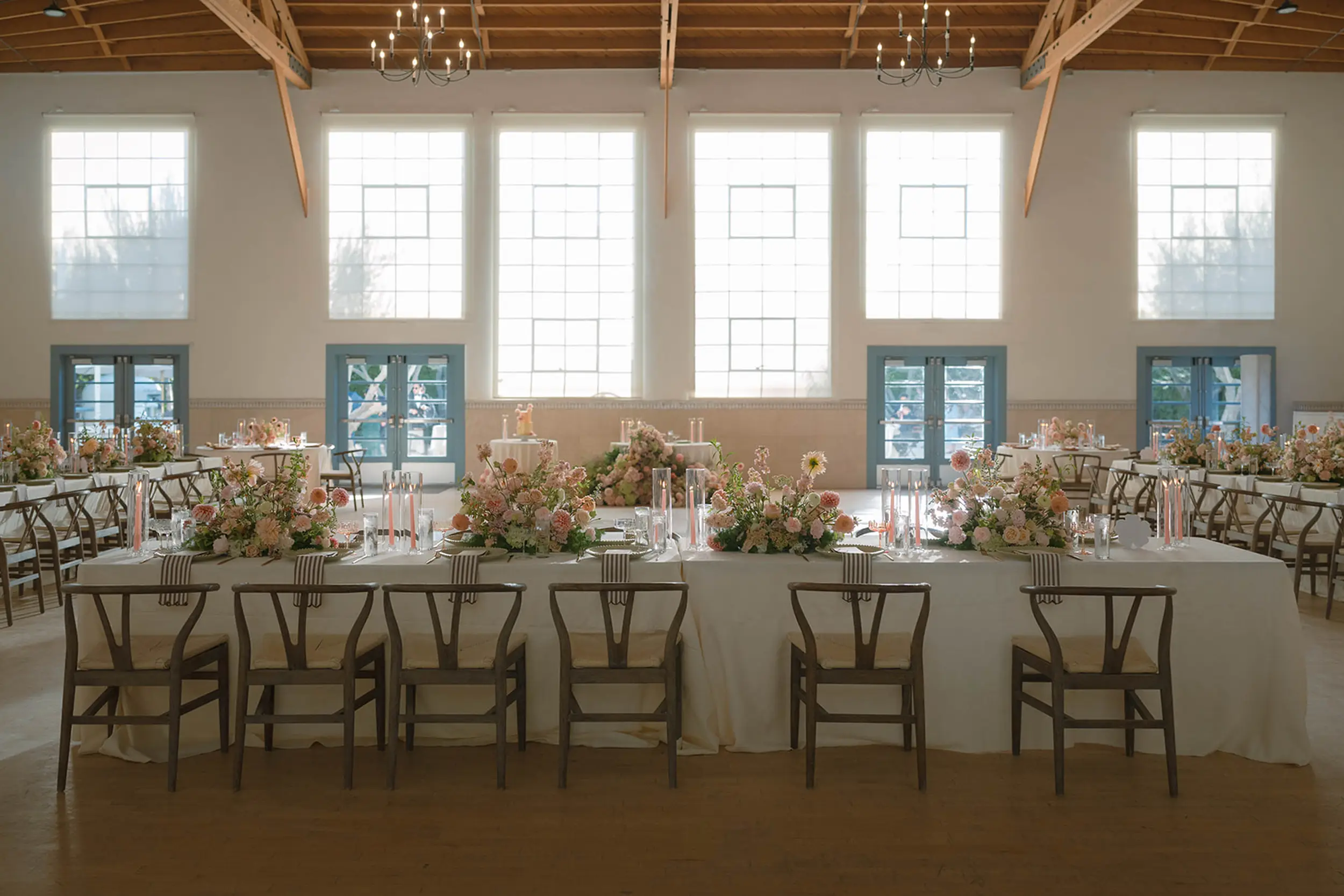Inside Grand Gimeno, reception tables are set with blush floral centerpieces, striped napkins, sage and pink charger plates, and pink and taupe candlesticks.