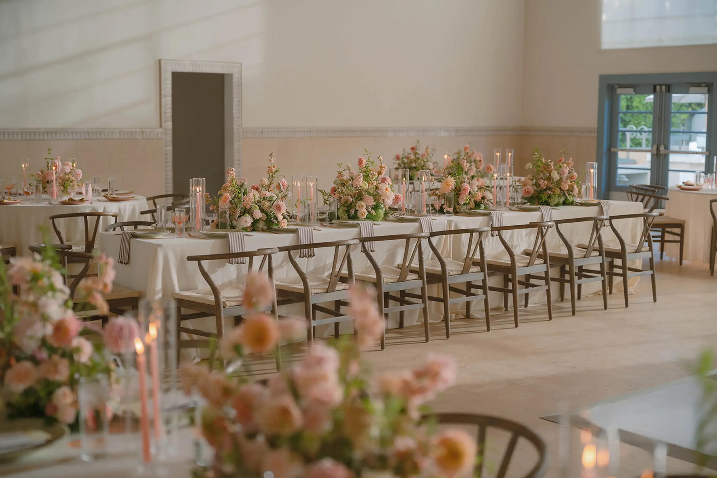 Inside Grand Gimeno, reception tables are set with blush floral centerpieces, striped napkins, sage and pink charger plates, and pink and taupe candlesticks.