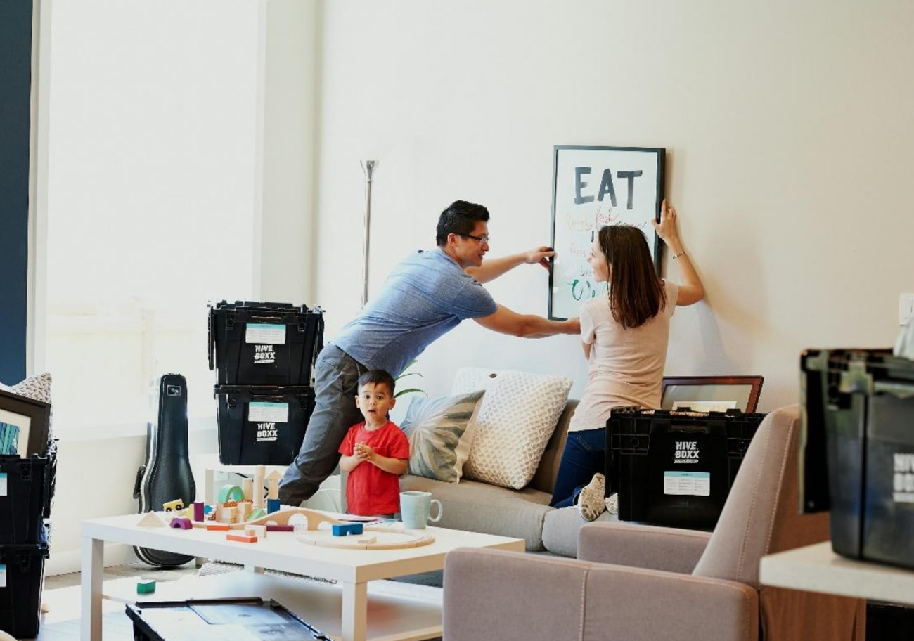 A family is unpacking boxes in their new home, surrounded by moving supplies and smiling as they settle in. 