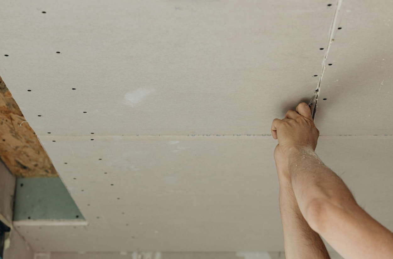 A man holds a screwdriver while reaching up to make adjustments to the ceiling.