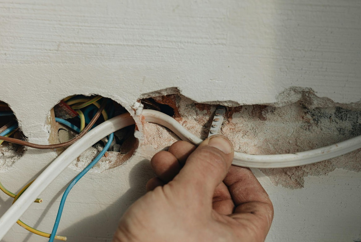 An individual is fixing wires to a wall, ensuring proper installation and management of electrical connections.