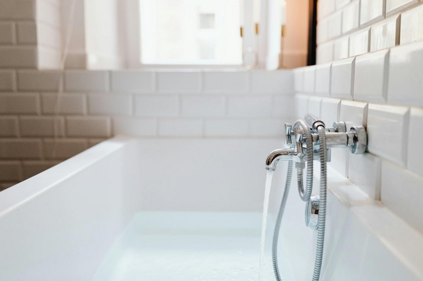 A white bathtub with a chrome faucet and shower head, set against a neutral bathroom backdrop.
