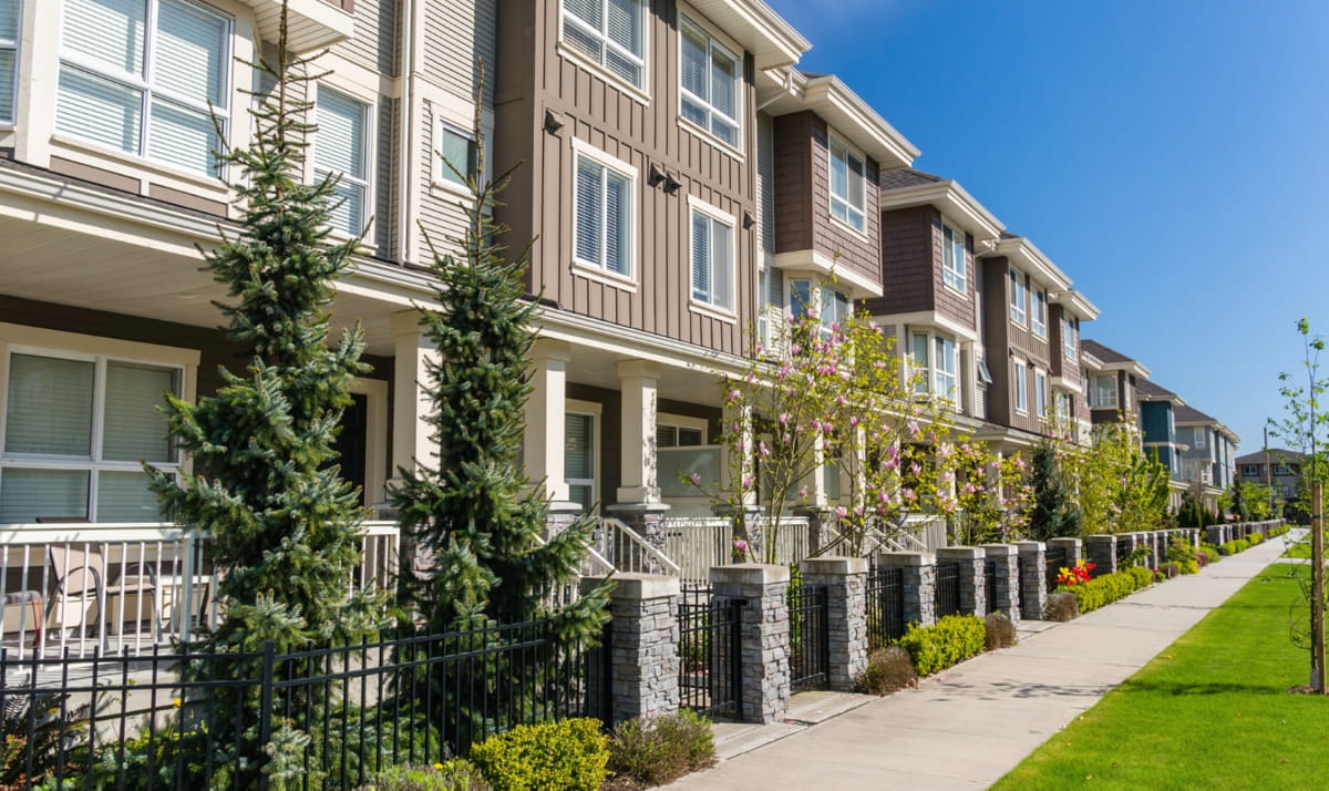 A row of townhouses bordered by a fence, with a grassy area in front, showcasing a suburban neighborhood setting.
